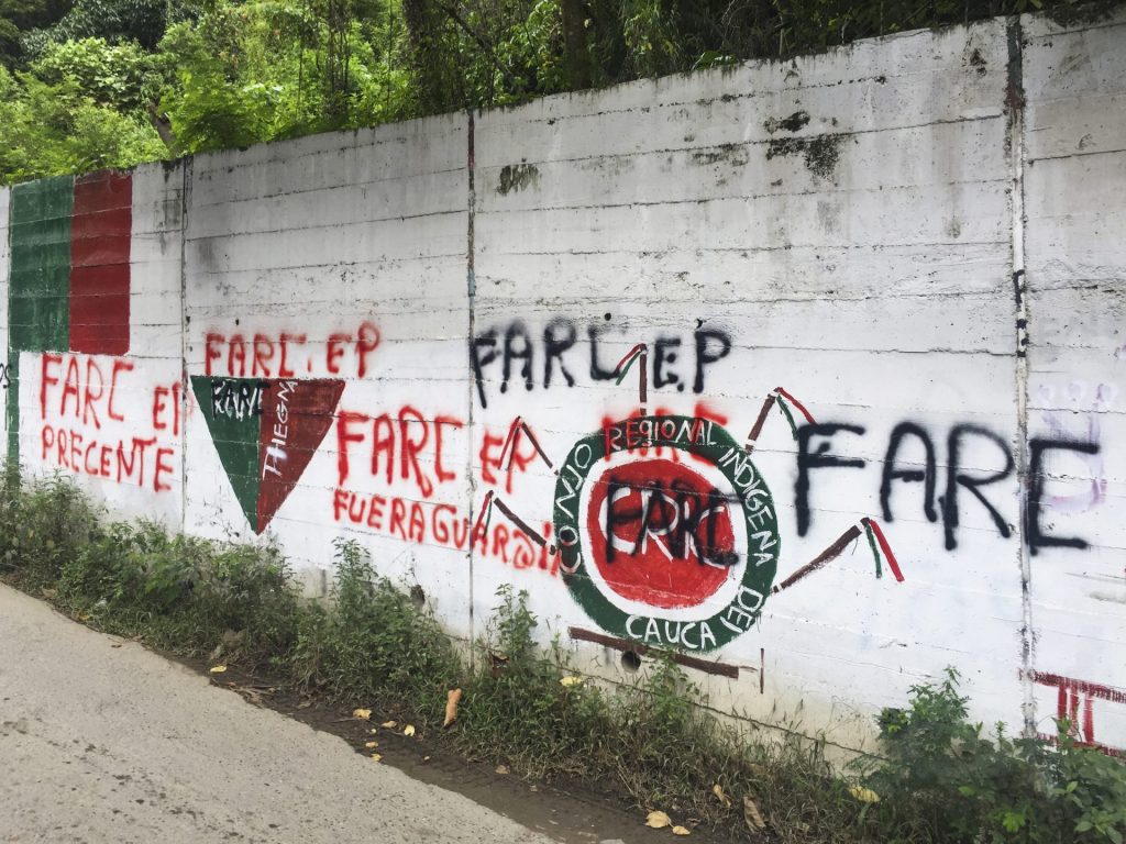 Su un muro bianco ci sono una serie di murales verdi e rossi fatti dai gruppi armati. Sopra i murales ci sono scritte delle parole: Farc, Fuera Guardia, Conjo Regional Indigena.