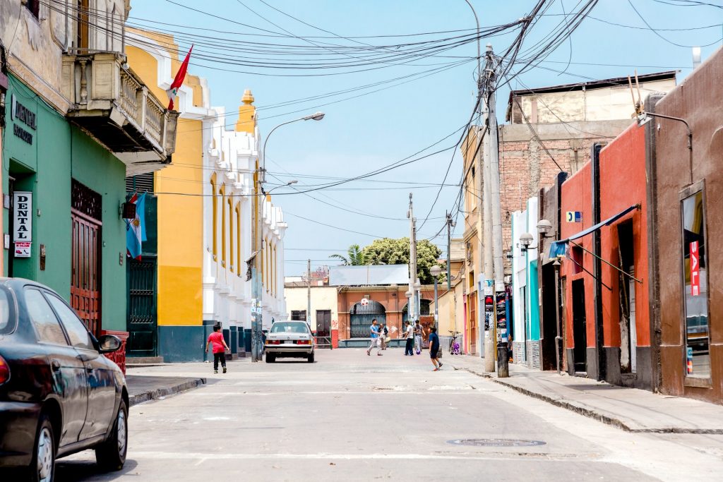 L'immagine è decorativa. È a Lima, di giorno, e ci sono delle strade sono quasi vuote, ad eccezione di alcuni bambini che giocano a palla. Le case sono colorate di colori vividi, rosso, giallo, verde, e incorniciano la scena.
