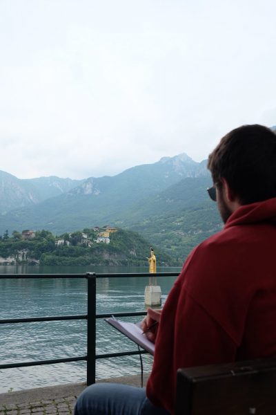 Giacomo Bonalana scrive seduto su una panchina in riva al Lago di Como