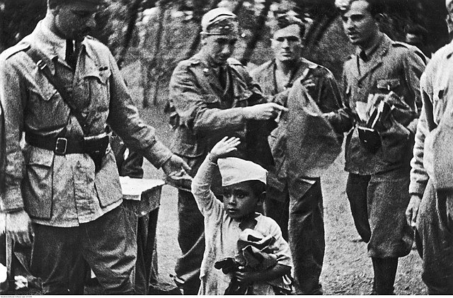 Bambino etiope che mostra il saluto romano circondato da soldati italiani, 1936-39